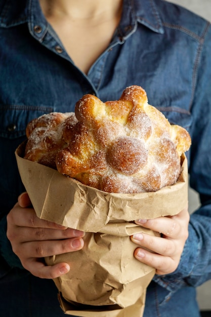 Traditional mexican bread of the dead "pan de muerto" in the young womans hands, blue background