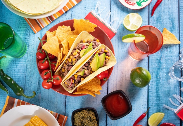 Traditional Mexican corn tacos with meat vegetables avocado beans salsa and nachos Served with various sauces and drinks Top view Big family gatherings