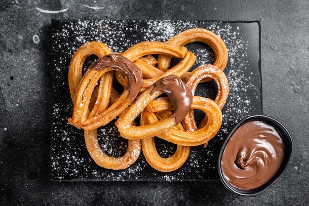 Traditional mexican dessert churros with chocolate sause. Black background. Top view.