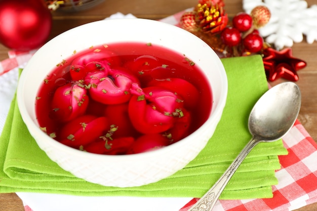 Traditional polish clear red borscht with dumplings and Christmas decorations on wooden table background