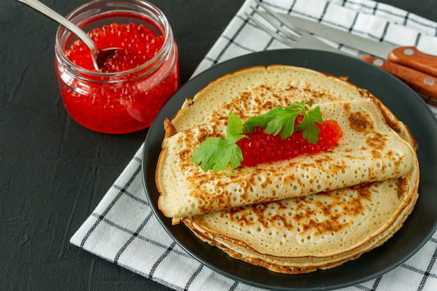 Traditional Russian Crepes Blini stacked in a plate with red caviar on wooden background. Maslenitsa traditional Russian festival meal. Russian food, russian kitchen. Close up.