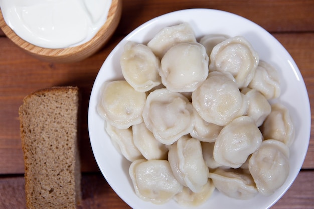 Traditional Russian dumplings with sour cream on a wooden background closeup