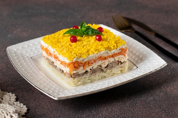 Traditional Russian salad Mimosa with canned fish potatoes cheese carrots and eggs on brown background