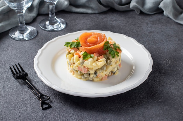 Traditional Russian salad Olivier with salted salmon on a dark gray background.