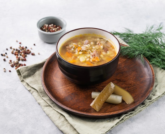 Traditional Russian soup with pickled cucumbers Pickle with pearl barley and meat on a light background with fresh dill and spices