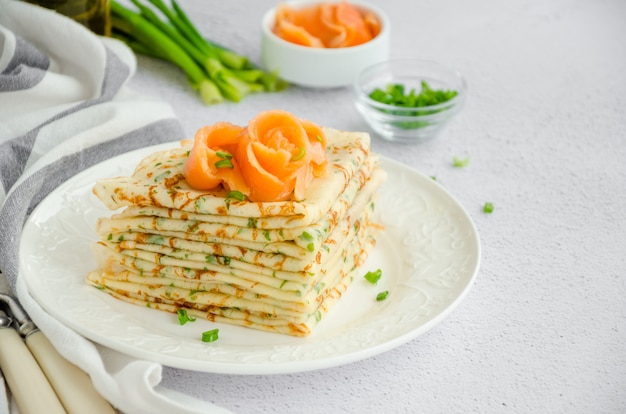 Traditional Russian thin pancakes or crepes with cheese, herbs and smoked salmon on a white plate on a light surface Holiday maslenitsa. Horizontal orientation