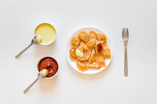 Traditional russian and ukrainian food vareniki dumplings with mustard and tomato sauce on a white plate.