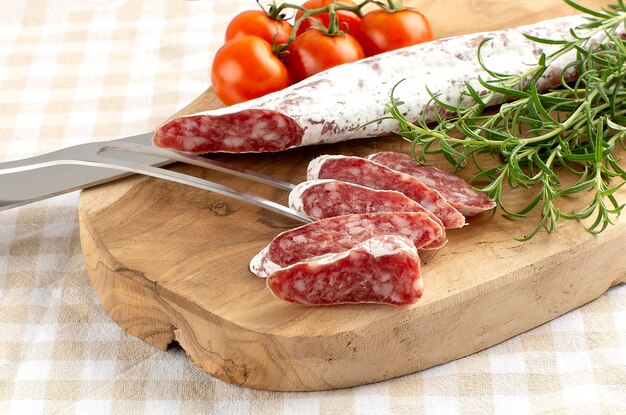 Traditional sausage cut into pieces with knife and fork with rosemary and spices on wooden cutting board on rustic background