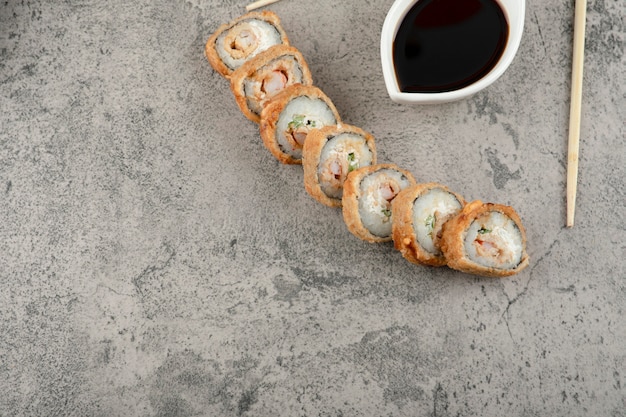 Traditional soy sauce and hot sushi rolls on stone background.