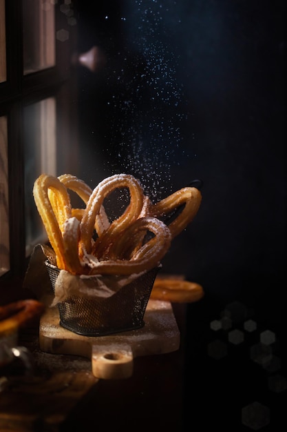 Traditional Spanish churros on the table. Dark and moody photo, rustic style. Magic light goes from the window