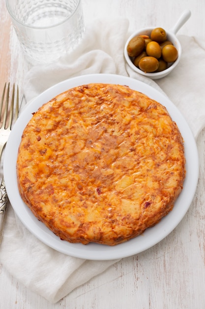 Traditional spanish food Tortilla with potato on white dish and olives in small bowl on ceramic background.