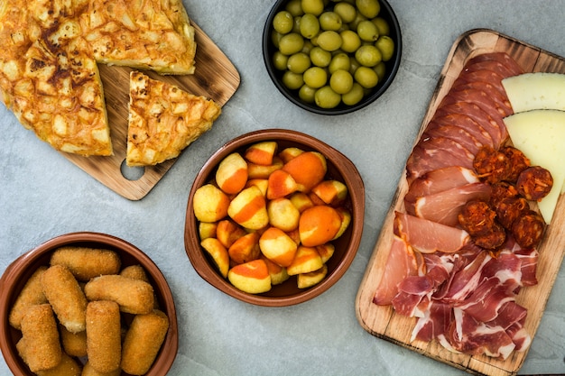 Traditional spanish tapas Croquettes, olives, omelette, ham and patatas bravas on gray stone