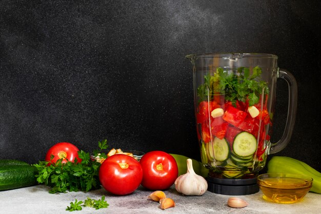 Traditional summer cold tomato soup gazpacho ingredients in a blender. Tomatoes, pepper, garlic, basil, parsley, olive oil and croutons. Mediterranean, Spanish cuisine. Black background. Copy space