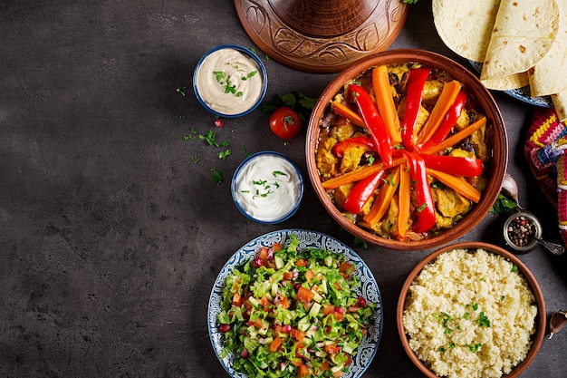 Traditional tajine dishes, couscous and fresh salad  on rustic wooden table.