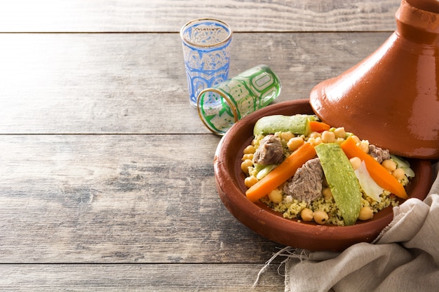 Traditional tajine with vegetables, chickpeas, meat and couscous on wooden table.