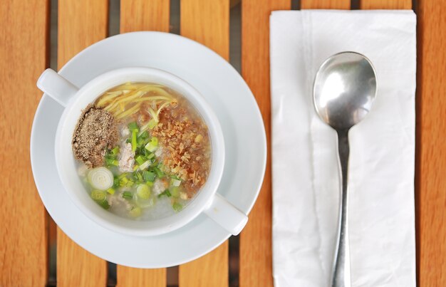 Traditional Thailand porridge rice gruel in cup on wooden table with spoon and tissue.