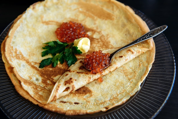 Traditional thin Russian pancakes with red caviar, butter and greens