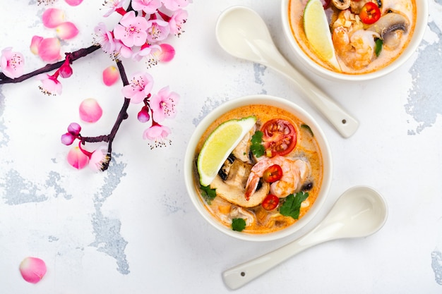 Traditional Tom Yum soup with blooming sakura branch on white stone table