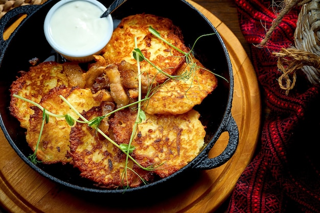 Traditional Ukrainian deruny with sour cream in a black pan Ukrainian cuisine Potato pancake Close up