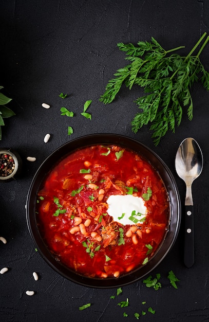 Traditional Ukrainian Russian borscht with white beans on the black bowl and ingredients for borsch. Flat lay. Top view.