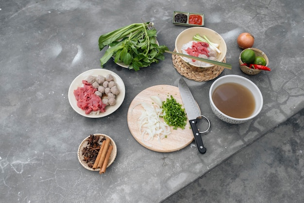 Traditional Vietnamese soup Pho bo with herbs, meat, rice noodles, broth. Pho bo in bowl with chopsticks, spoon. Space for text. Top view. Asian soup Pho bo on wooden table background. Vietnamese soup