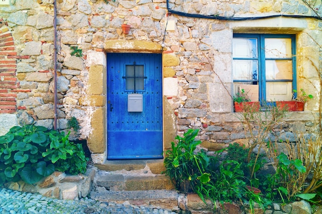 Traditional wooden medieval vintage blue painted doors and window in Tossa de Mar Spain Catalonia Costa Brava Green plants  near antique stone wall