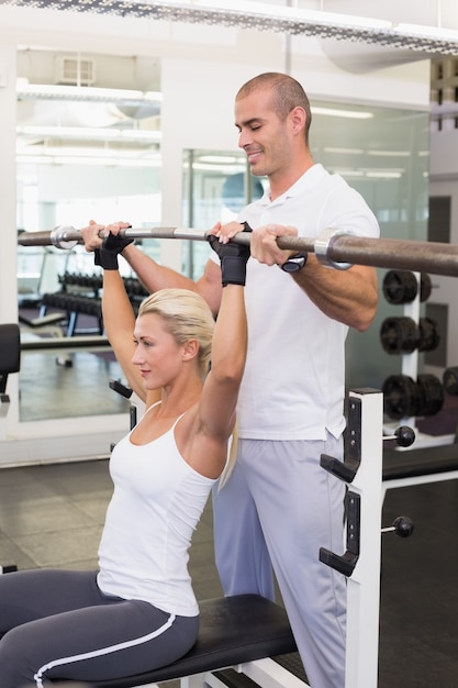 Trainer helping woman with lifting barbell in gym