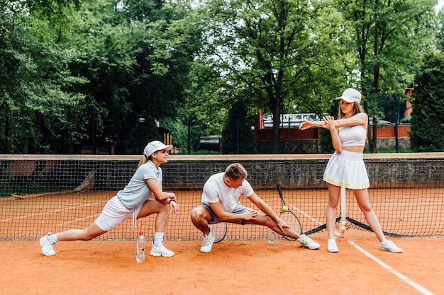 Trainer  male tennis player and two woman stretches before playing. Young team together.