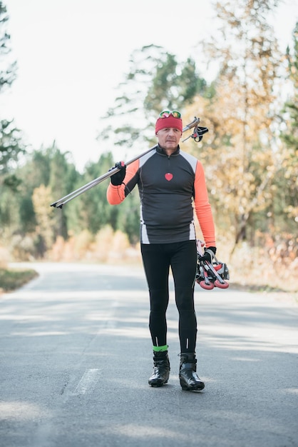 Training an athlete on the roller skaters Biathlon ride on the roller skis with ski poles in the helmet Autumn workout Roller sport The athlete goes and holds sports equipment in his hand