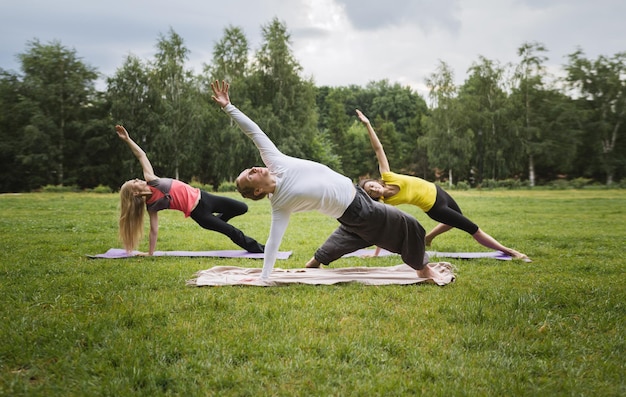 Training in park - instructor shows flexibility exercise for group of girls in park, early morning