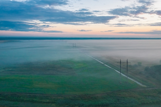 Tranquil morning landscape with fog and power line in the field