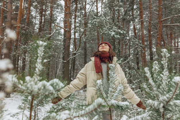 Tranquil woman in warm outerwear standing with outstretched arms in snowy forest