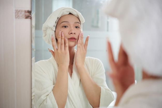 Transgender woman in bathrobe applying moisturizing lotion after morning shower