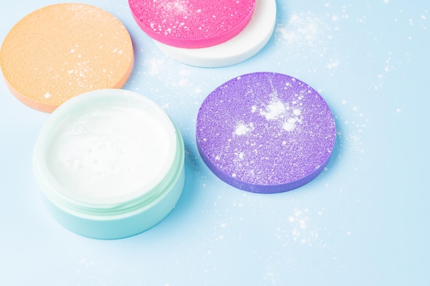 Translucent powder in green jar with makeup sponges on blue background Close up