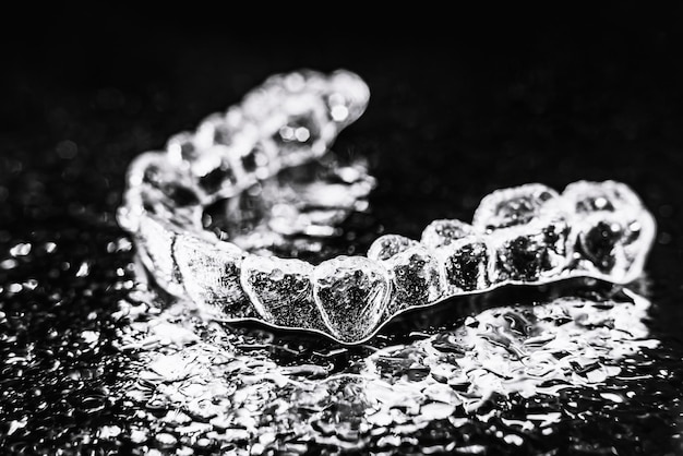 Transparent aligners tooth retainers lie on a mirror with water droplets on a black background