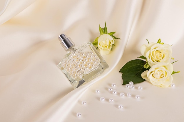 A transparent bottle of cosmetic spray or perfume filled with beautiful pearls lies on the folds of beige satin fabric Creative composition