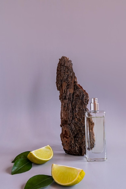 A transparent bottle of perfume on a beige background opposite the bark of the tree and lime slices trend concept of natural materials and smells