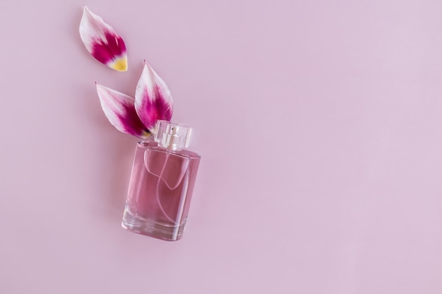 A transparent bottle of perfume or toilet bowling water on a purple background with tulip petals top view a copy of the space