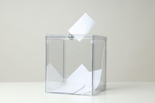 Transparent box and voting papers on gray background