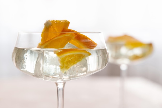 Transparent cocktail with ice cubes in a glass decorated with slices of orange close up