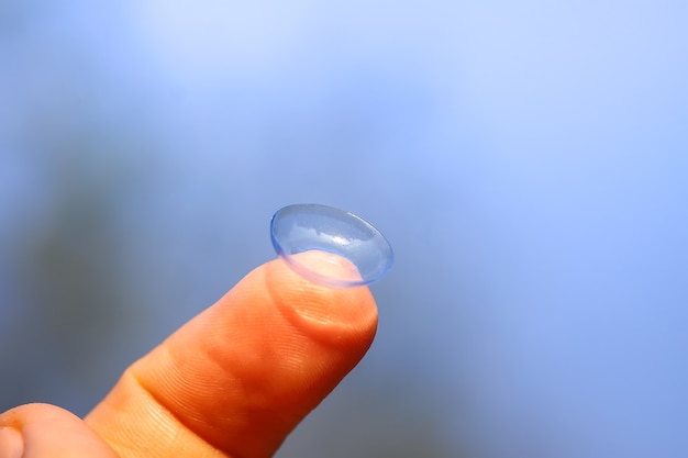 Photo transparent contact lens on finger tip on blurred green summer nature background.