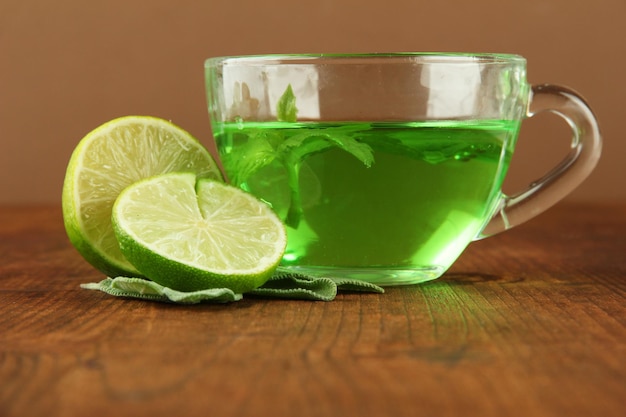 Transparent cup of green tea with lime and sage on table on brown background