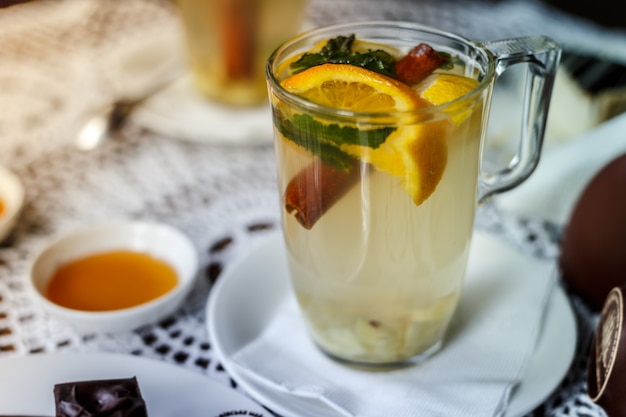 Transparent cup of tea with cinnamon, mint, orange on the table with a honey. 