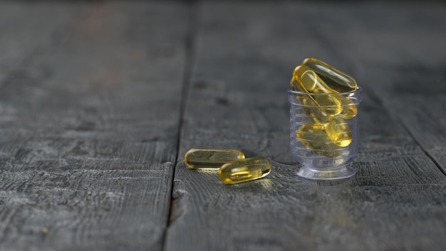 A transparent cup with fish oil capsules on a wooden table