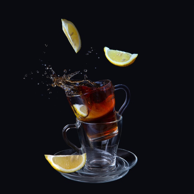 Transparent cups with tea. Lemon slices fall into the cup. Bursts, splashes. 