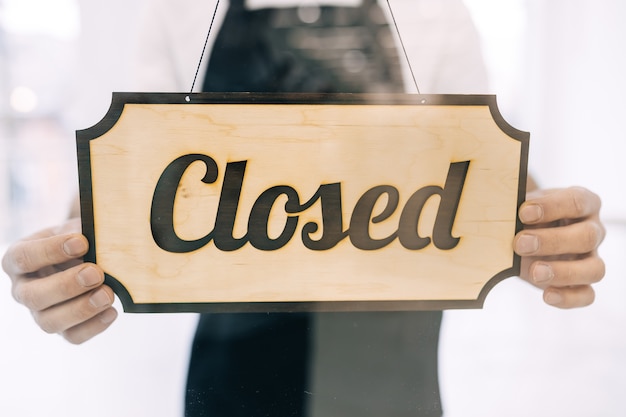 Transparent door with hands holding a closed signboard