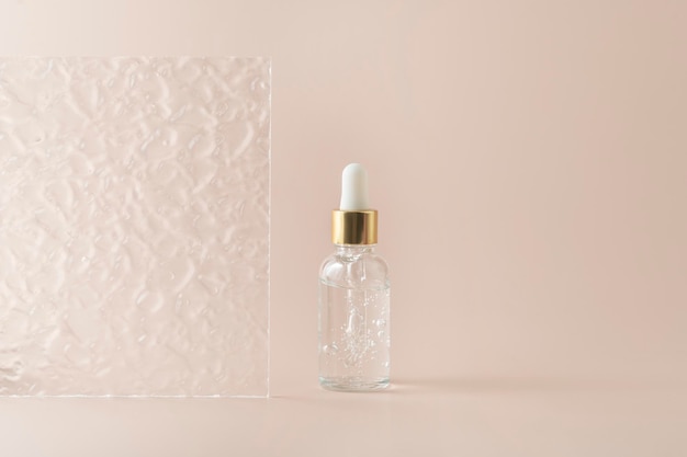 A transparent face serum in dropper bottle or essential oil or gel standing on a beige background