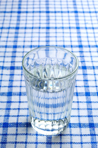 Transparent faceted glass of water on a blue tablecloth