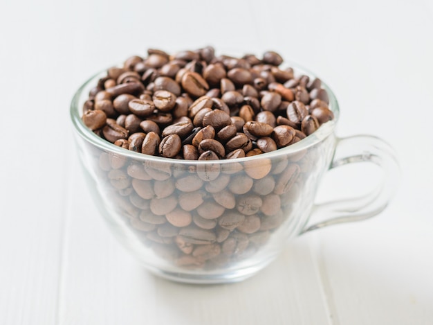 Transparent glass bowl filled with coffee beans on white wooden table.