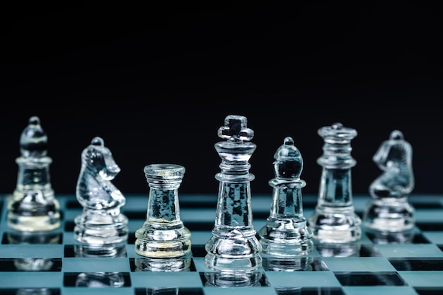 Transparent glass chess pieces arranged in a row reflecting in glass chessboard Isolated on black